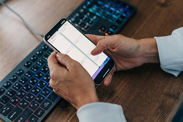 istock Close-up  hands using a mobile phone at a desk in the workplace typing plans in an electronic organizer. 2246374225