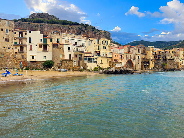 Beach of golden sand and crystal-clear waters, right next to the historic center, next to the medieval walls and the imposing Rocca di Cefalù, Palermo, Sicily, Italy, August 27, 2025