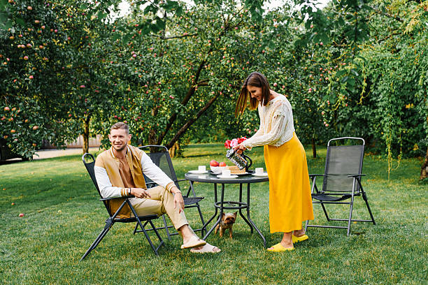 Family enjoying tea and fresh air together in a sunny garden, sitting by the table with flowers and fruits. Perfect for lifestyle, leisure, and family themes.