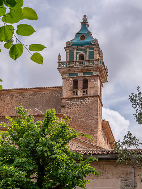 istock Kartause, Valldemossa, Mallorca, old stone bell tower with a green dome and intricate balcony stands against a partly cloudy sky, surrounded by lush green foliage, Majorca 2246383090