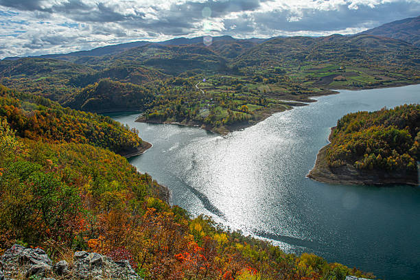 istock Sunlit Lake Reflecting Between Autumn Hills and Green Fields Under a Dramatic Cloudy Sky in the Mountains 2246384101