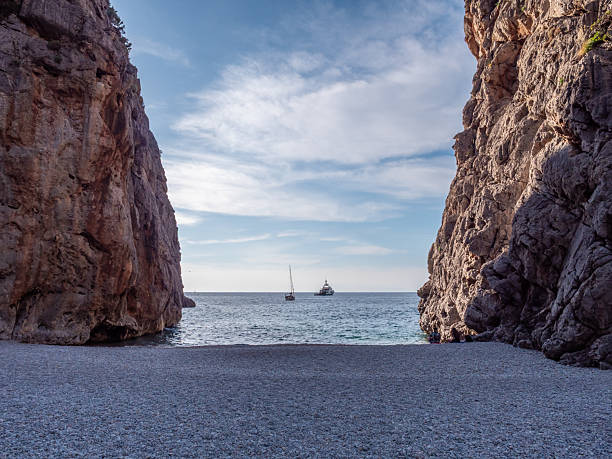 istock Sa Calobra, Mallorca, serene beach nestled between towering cliffs, with a sailboat gliding across the calm sea under a partly cloudy sky, majorca 2246385173