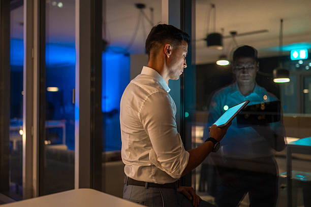 istock Contemplative Asian Businessman Using Tablet by Office Window in Evening Light 2246390349