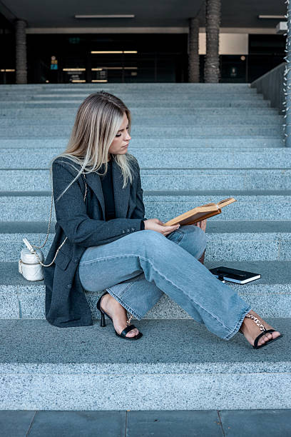 istock Woman reading a book while sitting on outdoor steps in a modern setting 2246394121