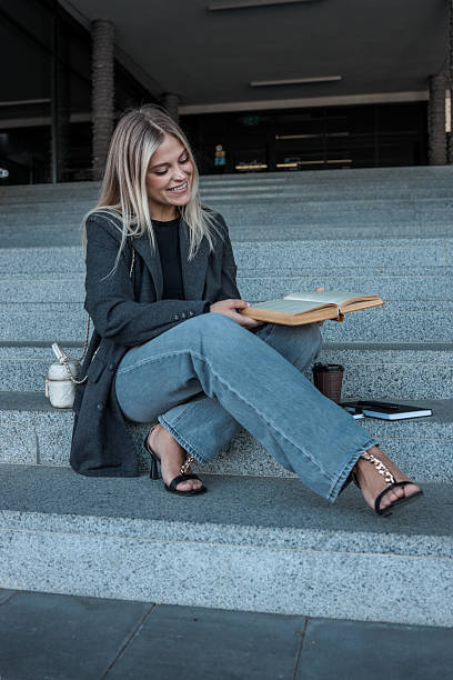 istock Young woman reading a book while sitting on outdoor steps 2246394127