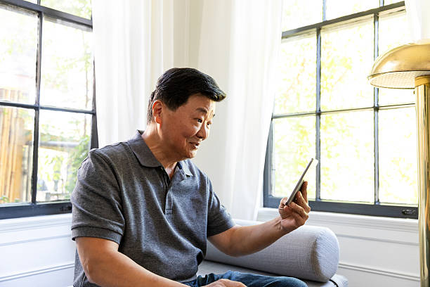 istock Elderly Asian man smiling while looking at a digital tablet in a bright room 2246399195
