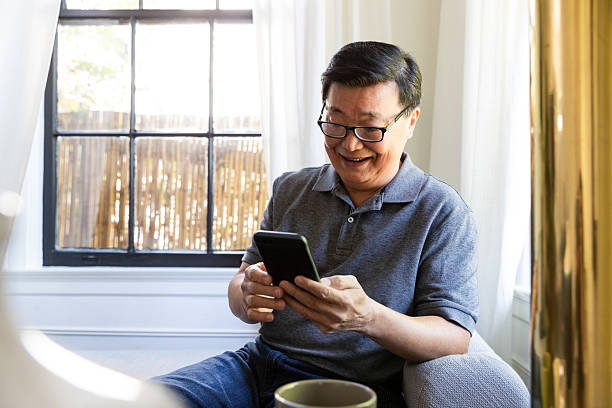 istock Asian man laughing while using his smartphone near a window indoors 2246399198