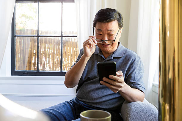 istock Asian man wearing glasses using a smartphone, seated indoors near a window. 2246399203