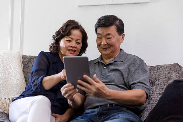 istock Elderly Asian couple smiling while looking at a digital tablet together indoors. 2246399209
