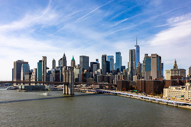 Bustling New York City showing the iconic Brooklyn Bridge connecting to Manhattan skyscrapers and buildings glistening during daytime. Panoramic New York city skyline featuring Brooklyn Bridge, Manhattan skyline and East River.