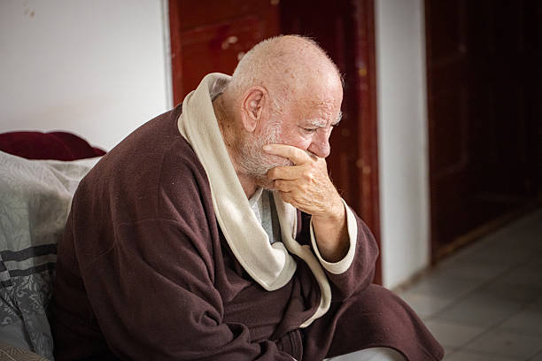Portrait of a senior man with Alzheimer’s Disease sitting at the chair, looking confused.
