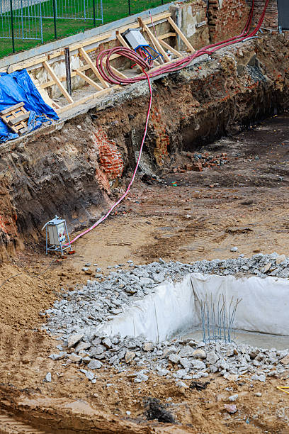 istock Excavation site beside modern residential buildings, showing a deep foundation pit with exposed soil layers, support beams, cables, and a blue tarp covering materials along the construction area 2246415119