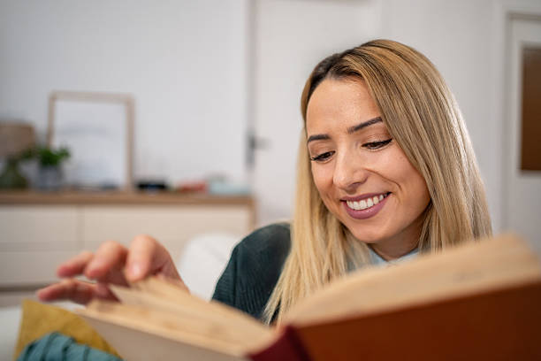 istock Woman smiling and relaxing while reading book at home 2246415552