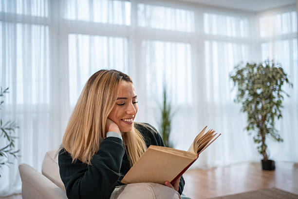 istock Young woman smiling while enjoying reading book at home 2246415558