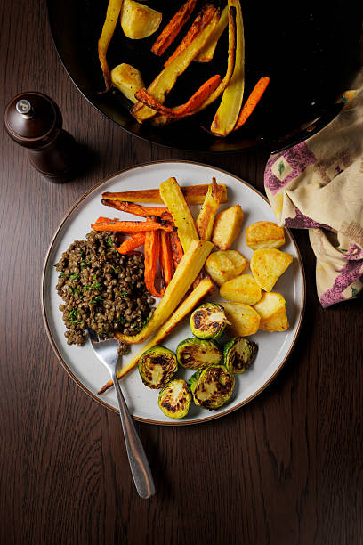 Top view of a Christmas roasted dinner for a vegan diet, featuring roasted potatoes, carrots, and parsnips, served with pan-grilled sprouts and miso green lentils.
