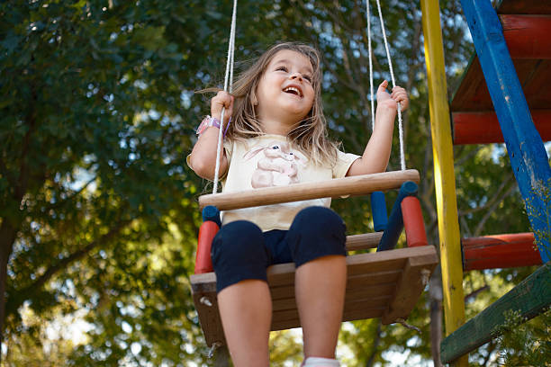 Girl enjoying playtime on a swing outdoors at a playground.