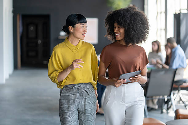 istock Two businesswomen walking and talking in modern office using digital tablet 2246430668