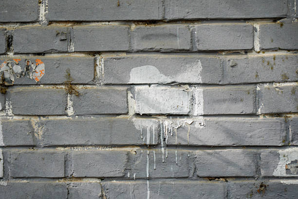 A weathered gray brick wall showing paint drips and patches, highlighting its textured surface.