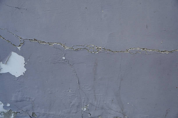 This image shows a close-up of a wall with visible cracks and peeling paint, indicating surface damage.