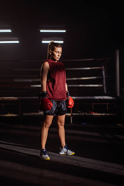 istock Female Boxer Stands Ready in the Ring, Focused Training Moment in a Dimly Lit Gym 2246436730