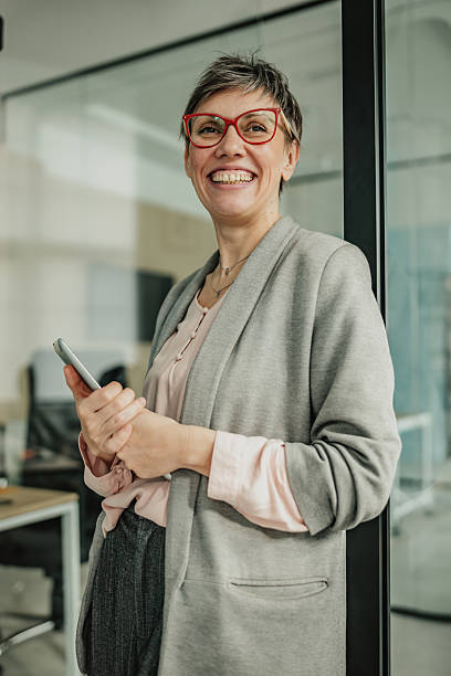 istock Businesswoman smiling and engaging in teamwork while standing in a modern office with a smartphone in hand 2246438398