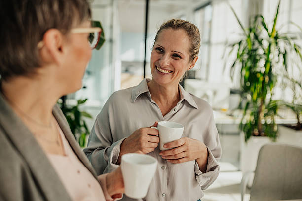 istock Businesswomen engaged in conversation while enjoying coffee in a bright, modern office setting 2246441947