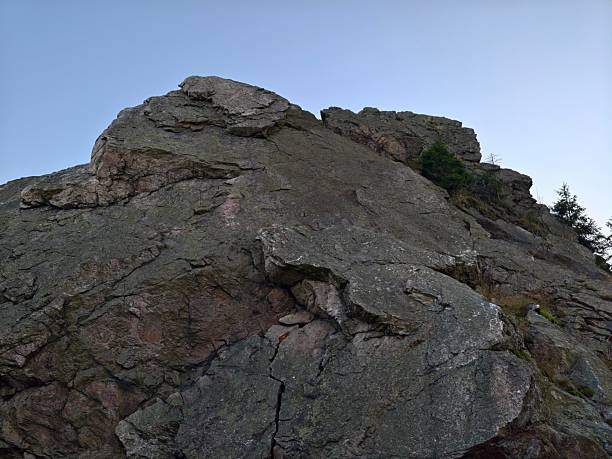 steep rocky summit face rising to clear sky, jagged crags and sheer exposure at top with rough fractured