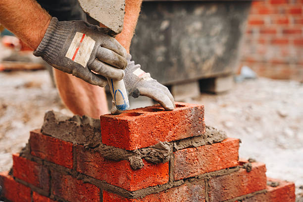 istock Close-up of builder bricklayer laying red bricks to form a house corner on building site 2246454371