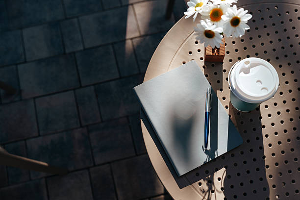 Notebook and coffee on a sunny table with flowers in a cozy outdoor setting