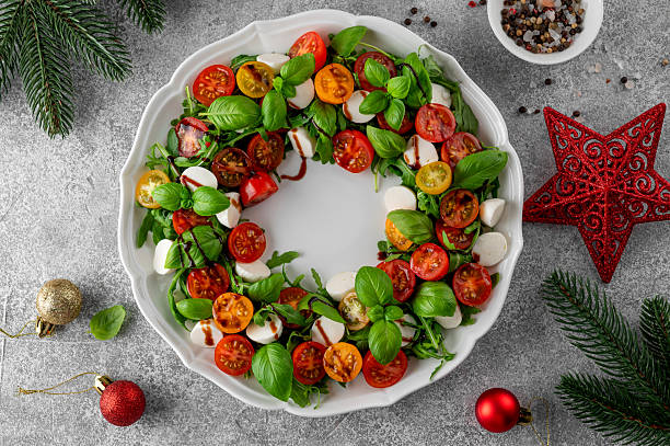 Christmas wreath Caprese salad with arugula, mozzarella, cherry tomatoes, fresh basil and balsamic glaze on a white plate on a gray concrete background. Top view.