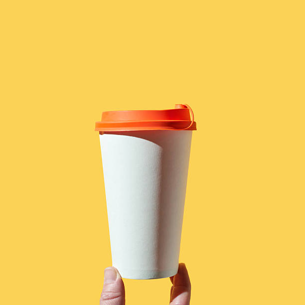 istock Hand holding coffee cup with orange lid on bright yellow background 2246460402