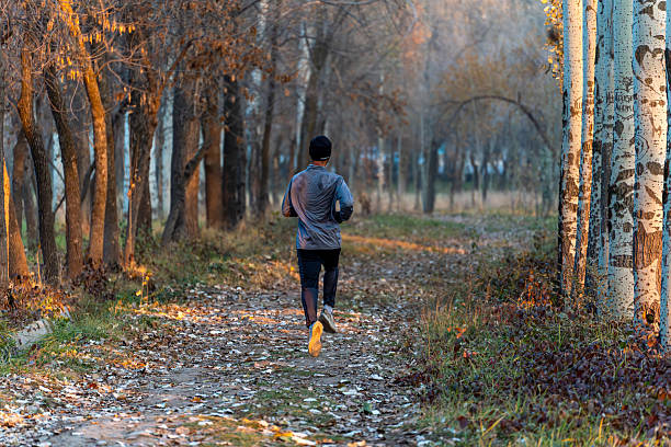 Bishkek, Kyrgyzstan - November 12, 2025: A lone runner from Central Asia is exercising on a dirt path in a park during the autumn season. The runner is wearing a long-sleeved gray and blue shirt, dark pants, and running shoes Nike.