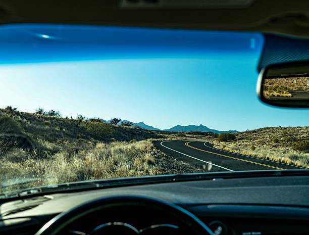 A captivating view of a winding road through a desert landscape captured from inside a car, showcasing the dashboard and rearview mirror. The clear blue sky and rugged terrain create a sense of adventure and freedom, ideal for travel, road trip, and outdoor lifestyle themes. This image evokes exploration and the open road, perfect for commercial use in travel, automotive, and nature campaigns.