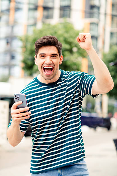 istock Young Man Celebrating Success Outdoors in a Modern Urban Environment on a Bright Sunny Day with Cheerful Energy 2246477294