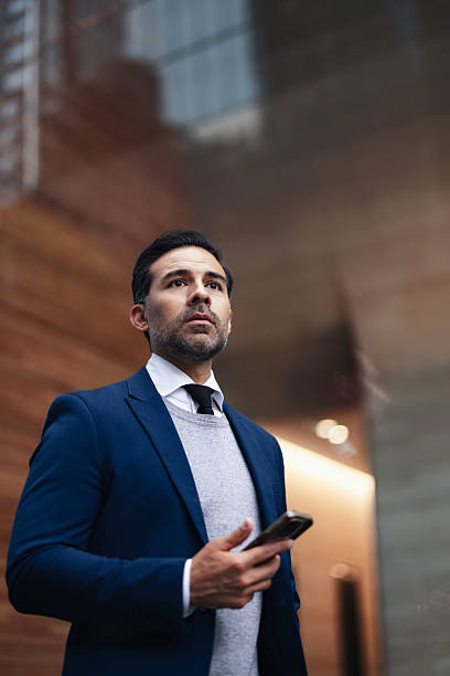 istock Professional Man In Blue Suit Looking Up While Holding Phone In Urban Outdoor Setting 2246482459