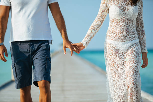 Young couple walking holding hands along jetty at Dhiffushi Holiday island, South Ari atoll, Maldives. Model and Property released. Hi resolution photo.