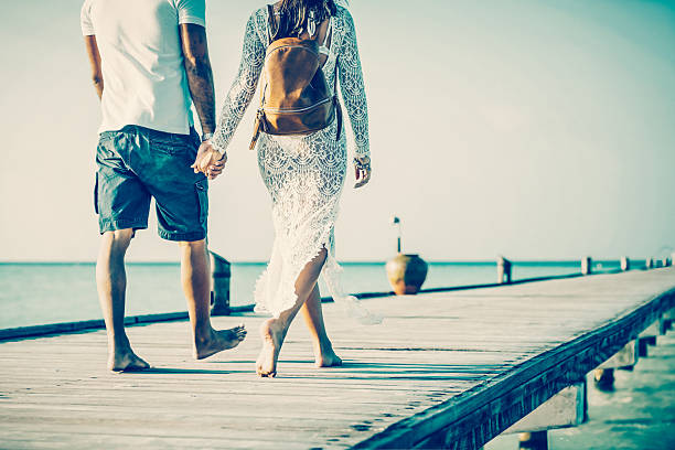 Young couple walking holding hands along jetty at Dhiffushi Holiday island, South Ari atoll, Maldives. Model and Property released. Hi resolution photo.