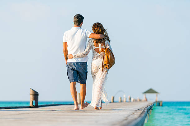 Young couple walking embraced along jetty at Dhiffushi Holiday island, South Ari atoll, Maldives. Model and Property released. Hi resolution photo.