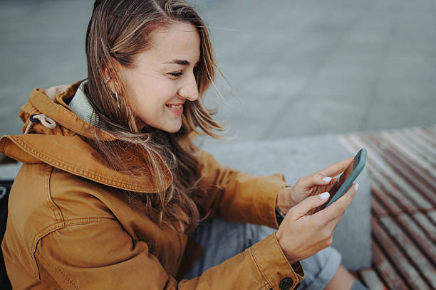 istock Young casually dressed woman using smartphone while sitting on bench in city 2246483172