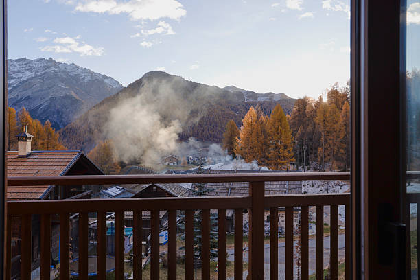 Sunrise over mountains and village from chalet deck in autumn, golden larches in distance, European Alps