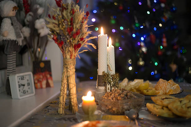 A warm holiday table set with beeswax candles, a traditional sheaf of dried grains, and a glass bowl of kutia beside winter fruit and pastries, creating a peaceful, mindful ambiance that supports themes of wellness and mental wellbeing.