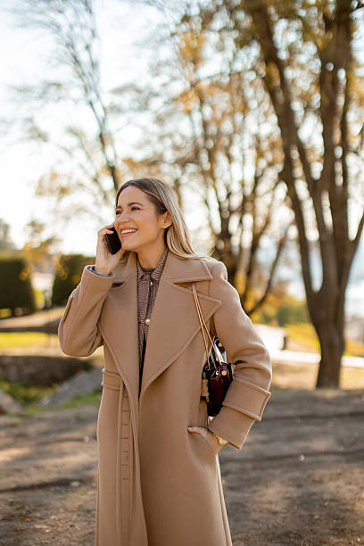 istock Woman in a coat talking on the phone while walking in a park during autumn 2246484451