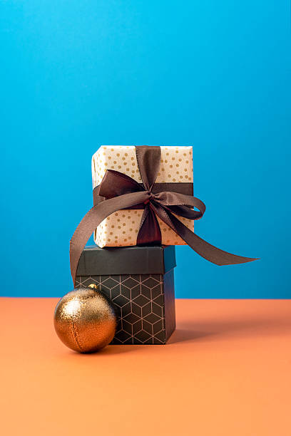 istock Stack of gift boxes with brown ribbon and golden bauble on blue and orange background. Christmas concept. Closeup 2246484555
