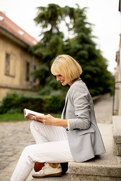 istock Woman sitting outdoors reading a book on a stone step in a tranquil setting 2246485650