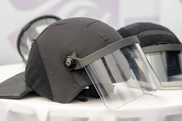 A police helmet with a transparent large visor is located on the table next to another protective helmet