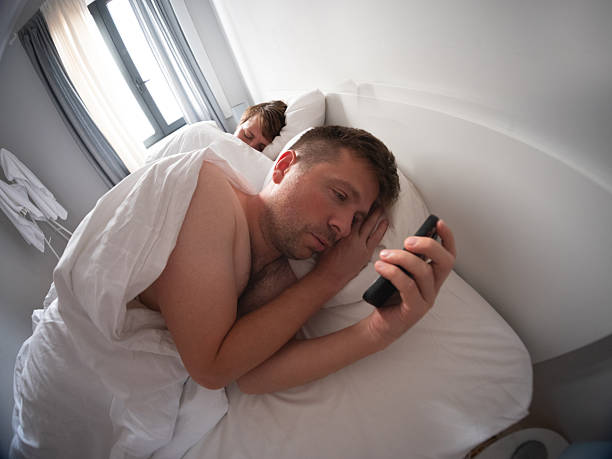 istock Man using his phone at night while his wife sleeps beside him 2246490059