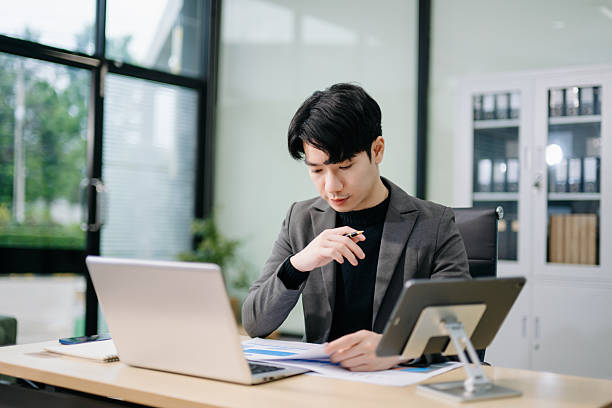istock Asian man using laptop and tablet while sitting at her working place. Concentrated at work. 2246498043