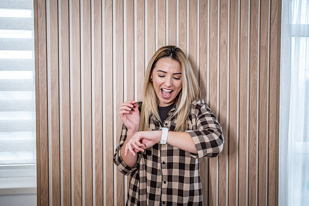 Young adult woman wearing a plaid flannel shirt checking time on her smartwatch, feeling shocked and stressed about being late for a deadline or important event