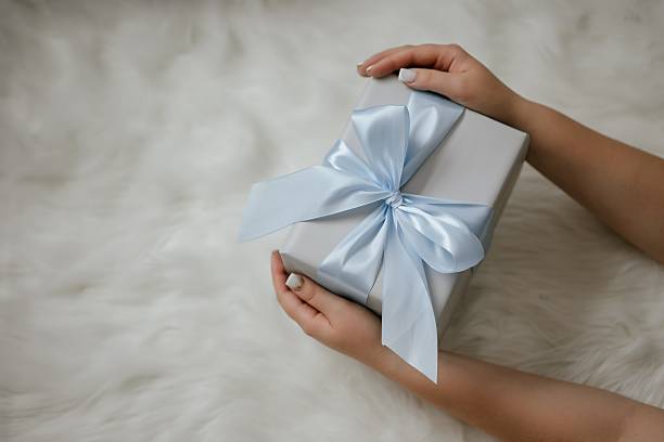 istock Hands Holding Gift Box with Blue Ribbon on Soft Surface 2246498803