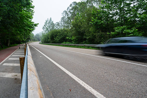 istock A blurry car is driving down a road with a fence on the side. 2246499202